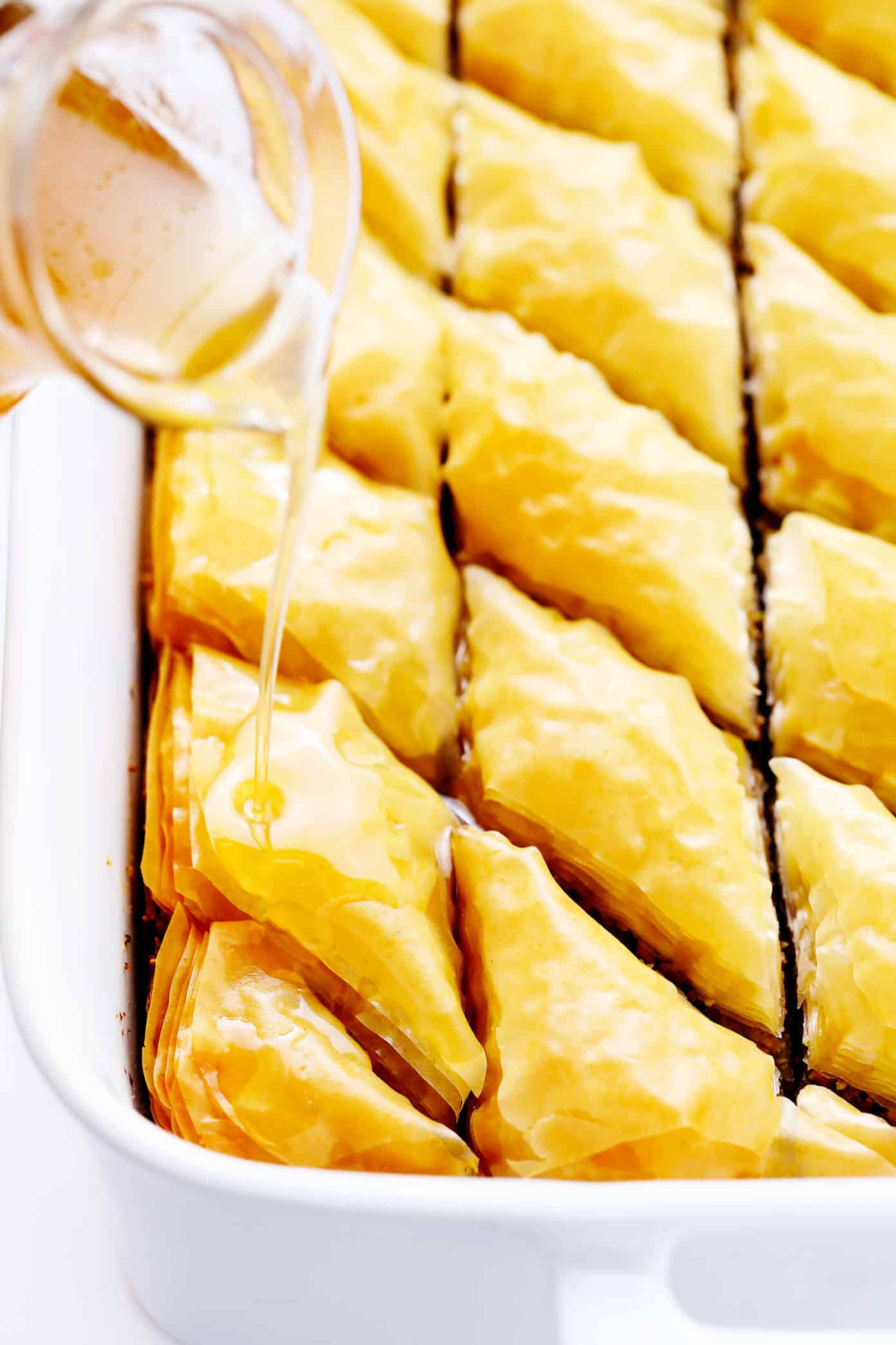 A step-by-step guide (and video) for how to make homemade baklava with perfectly crispy golden layers of buttery phyllo, pistachios and walnuts (or your choice of nuts), and lovely orange honey syrup. Always such a delicious treat! | gimmesomeoven.com Drizzling cold syrup on hot baklava