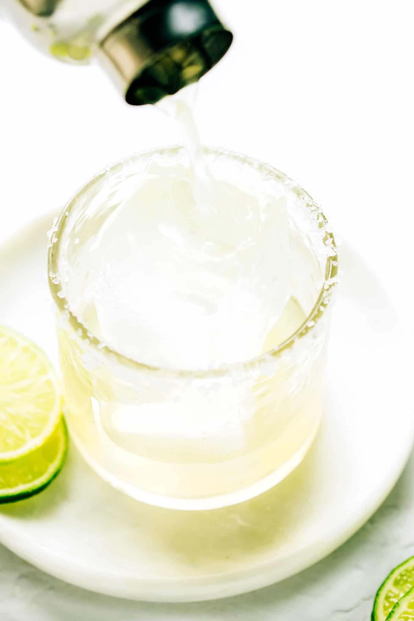 This bourbon margarita recipe swaps whiskey in place of the tequila in this classic cocktail...and it's so, so good. All you need is bourbon, freshly-squeezed lime juice, Cointreau (or your favorite orange liqueur), and maple syrup (optional sweetener) and this drink can be ready to enjoy in minutes. | gimmesomeoven.com Pouring a bourbon margarita into a salt-rimmed glass