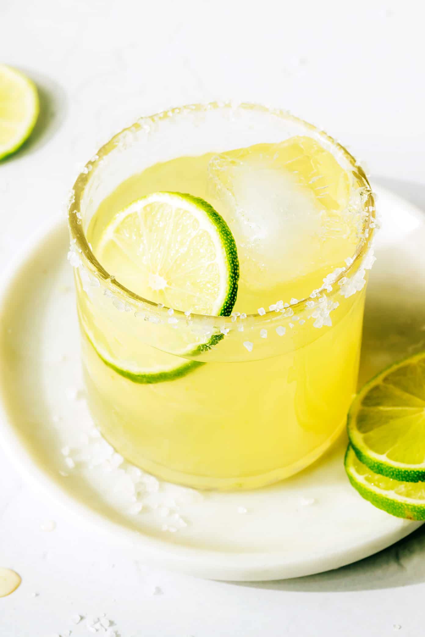 This bourbon margarita recipe swaps whiskey in place of the tequila in this classic cocktail...and it's so, so good. All you need is bourbon, freshly-squeezed lime juice, Cointreau (or your favorite orange liqueur), and maple syrup (optional sweetener) and this drink can be ready to enjoy in minutes. | gimmesomeoven.com Bourbon Margarita with a salt rim on a plate
