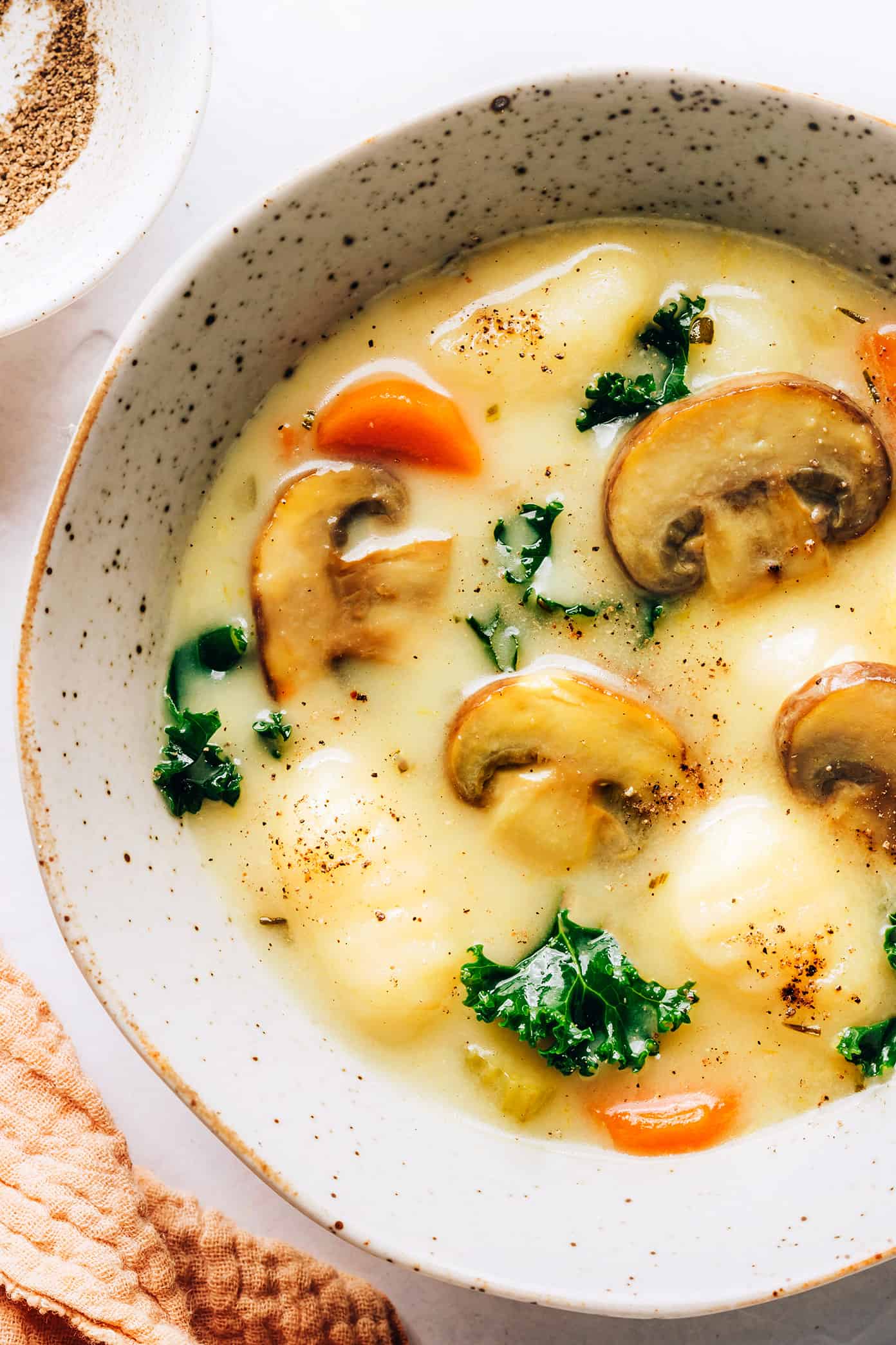 This gnocchi, mushroom and kale soup is made with a delicious creamy garlic-rosemary broth and topped with freshly-grated Parmesan. It's the perfect easy dinner recipe that comes together in under 30 minutes and always tastes so cozy and comforting. Feel free to keep the recipe vegetarian, or add in some Italian sausage, chicken or bacon too. | gimmesomeoven.com Closeup of creamy gnocchi, mushroom and kale soup