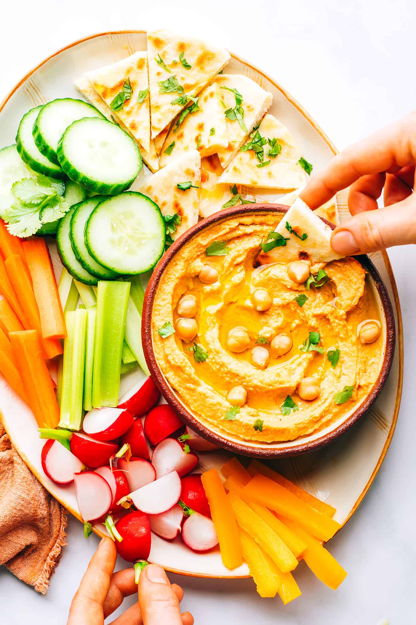This Thai-inspired red curry hummus recipe is quick and easy to make in just 10 minutes with chickpeas, tahini, coconut milk, curry paste, ginger and garlic. Serve it up as a dip with crudités and naan, or use it as a spread on burgers or wraps. Such a great easy appetizer! | gimmesomeoven.com Thai Red Curry Hummus on Platter with Crudites and Naan