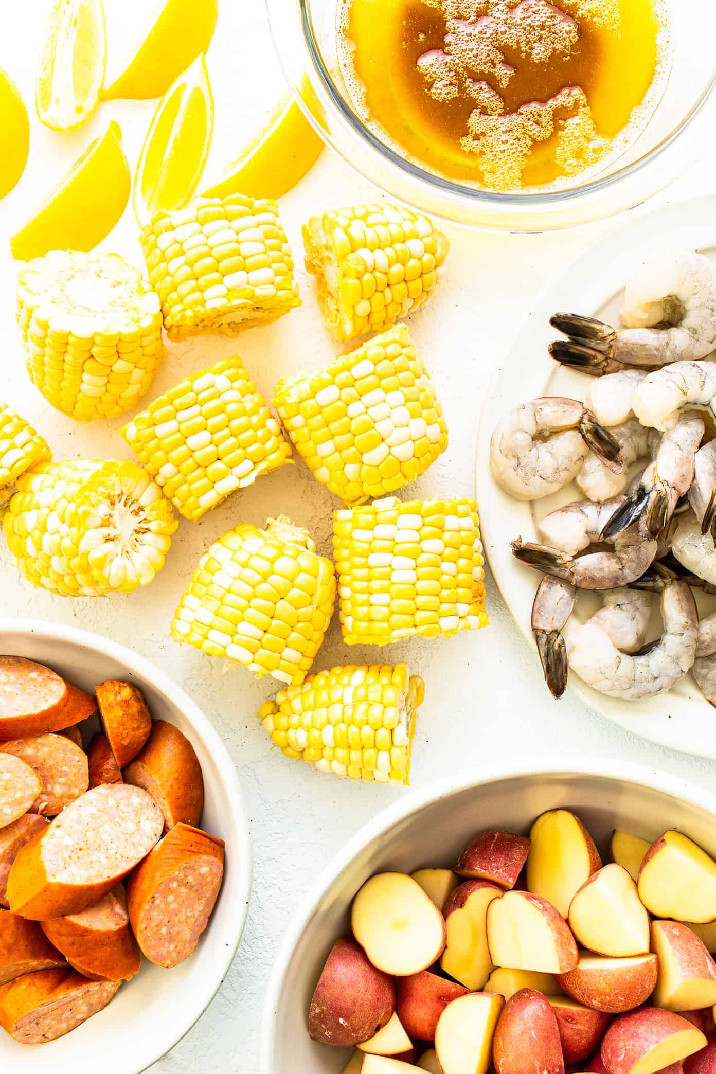 This classic shrimp boil recipe is super-easy to make with tender shrimp, sausage, potatoes, corn, zesty seasonings and a dreamy lemon garlic brown butter sauce. It's the perfect meal for easy entertaining and always a crowd fave! | gimmesomeoven.com Shrimp Boil Ingredients (lemon, corn on the cob, raw shrimp, Andouille sausage, red potatoes, brown butter)