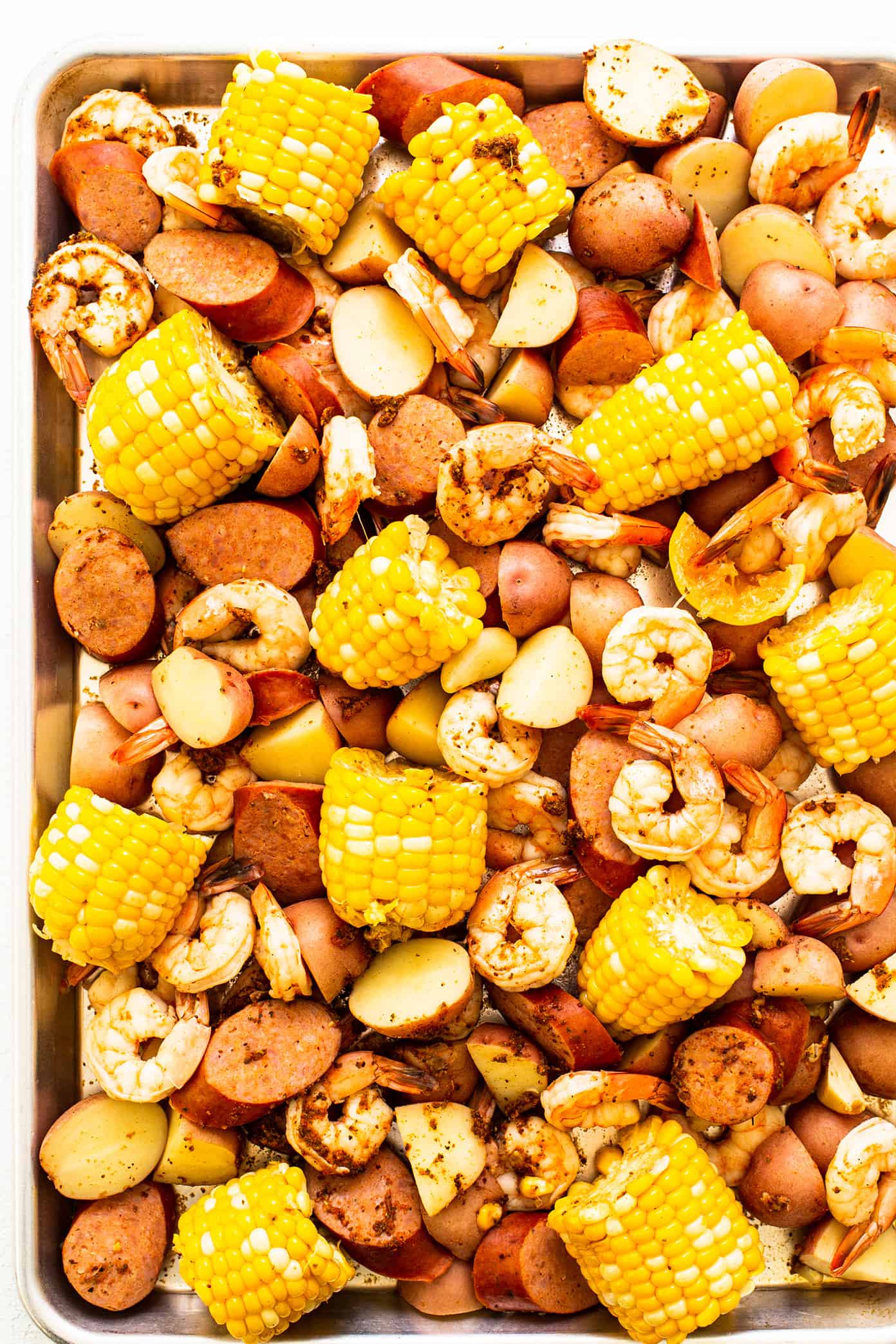 This classic shrimp boil recipe is super-easy to make with tender shrimp, sausage, potatoes, corn, zesty seasonings and a dreamy lemon garlic brown butter sauce. It's the perfect meal for easy entertaining and always a crowd fave! | gimmesomeoven.com Cooked shrimp boil on sheet pan