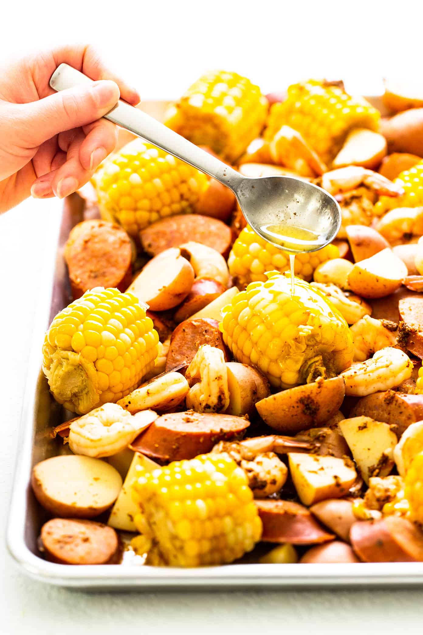 This classic shrimp boil recipe is super-easy to make with tender shrimp, sausage, potatoes, corn, zesty seasonings and a dreamy lemon garlic brown butter sauce. It's the perfect meal for easy entertaining and always a crowd fave! | gimmesomeoven.com Drizzling brown butter sauce on shrimp boil
