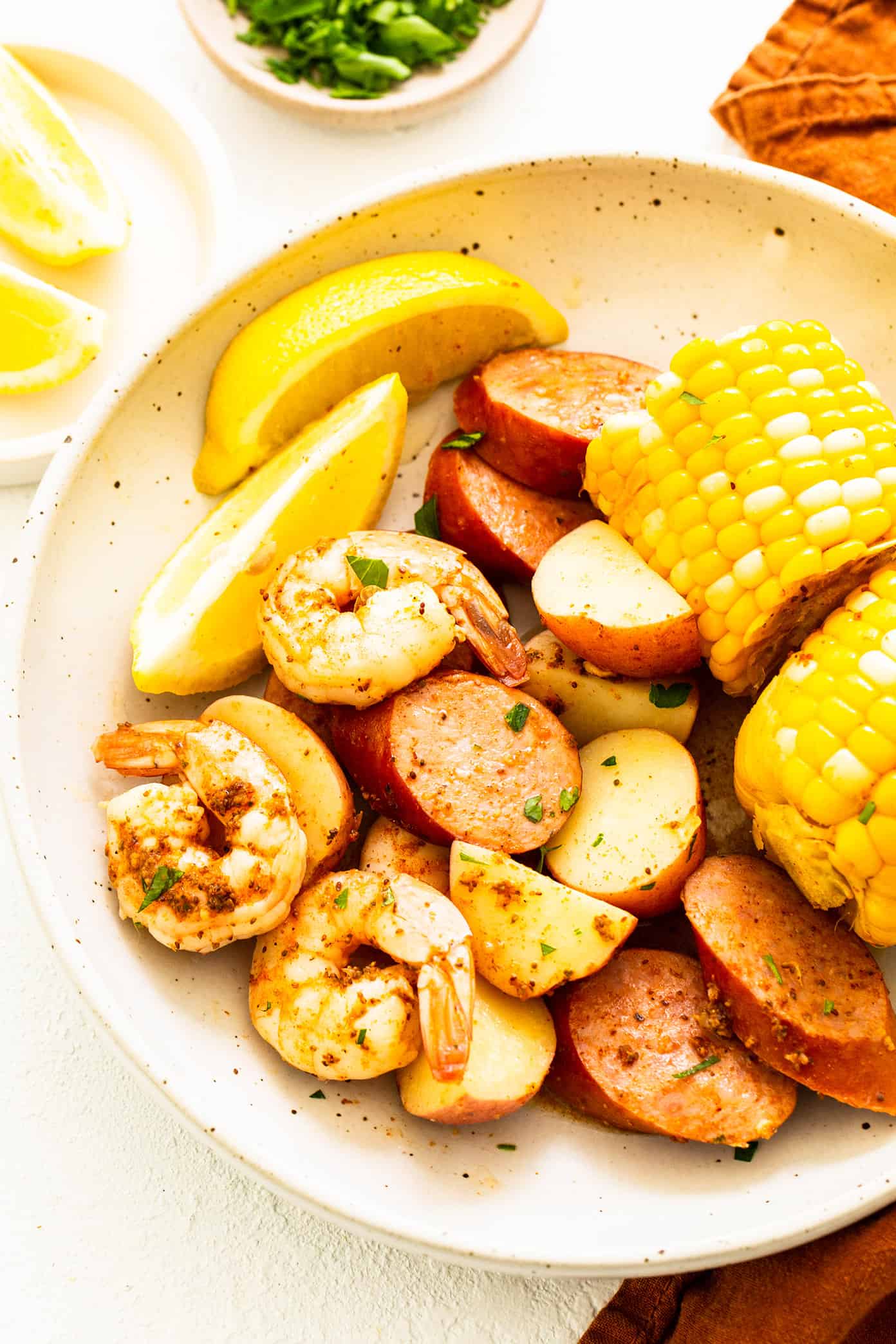 This classic shrimp boil recipe is super-easy to make with tender shrimp, sausage, potatoes, corn, zesty seasonings and a dreamy lemon garlic brown butter sauce. It's the perfect meal for easy entertaining and always a crowd fave! | gimmesomeoven.com Shrimp Boil on Serving Plate with Lemons
