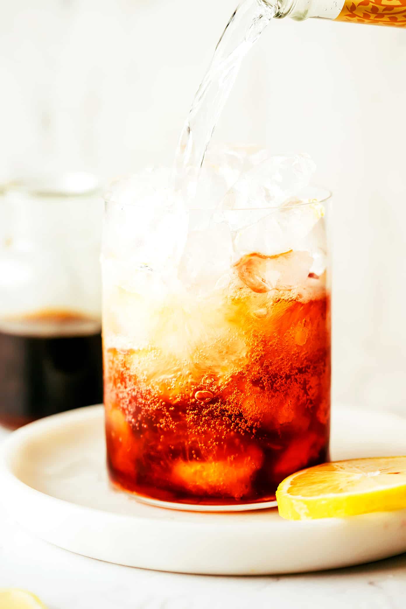 This cold brew tonic recipe is easy to make in a few minutes with three ingredients (cold brew coffee concentrate, tonic water, slice of lemon or orange, plus ice). Always such a refreshing, fizzy and delicious drink! | gimmesomeoven.com Pouring tonic water over cold brew concentrate and ice