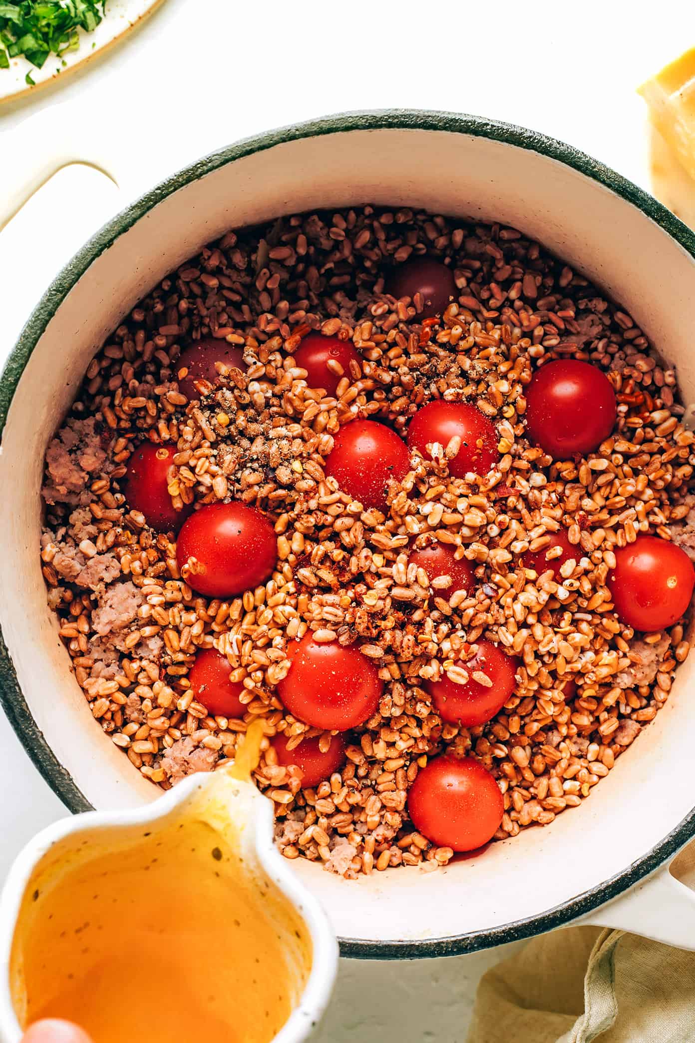 This one pot farro recipe is slow-simmered with Italian sausage, cherry tomatoes, fresh basil, garlic, spinach and finished with a sprinkling of pine nuts and Parmesan. Such an easy dinner recipe and always SO delicious. Feel free to use plant-based sausage to make it vegetarian too! | gimmesomeoven.com Adding broth to one pot farro with Italian sausage and tomatoes