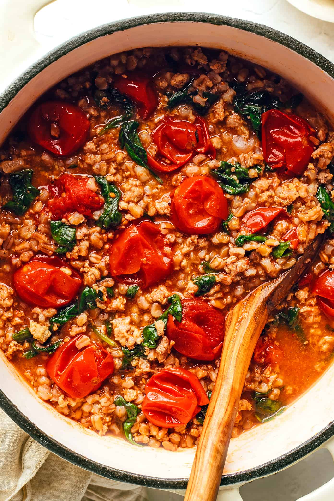 This one pot farro recipe is slow-simmered with Italian sausage, cherry tomatoes, fresh basil, garlic, spinach and finished with a sprinkling of pine nuts and Parmesan. Such an easy dinner recipe and always SO delicious. Feel free to use plant-based sausage to make it vegetarian too! | gimmesomeoven.com One Pot Farro with Italian Sausage and Tomatoes Closeup