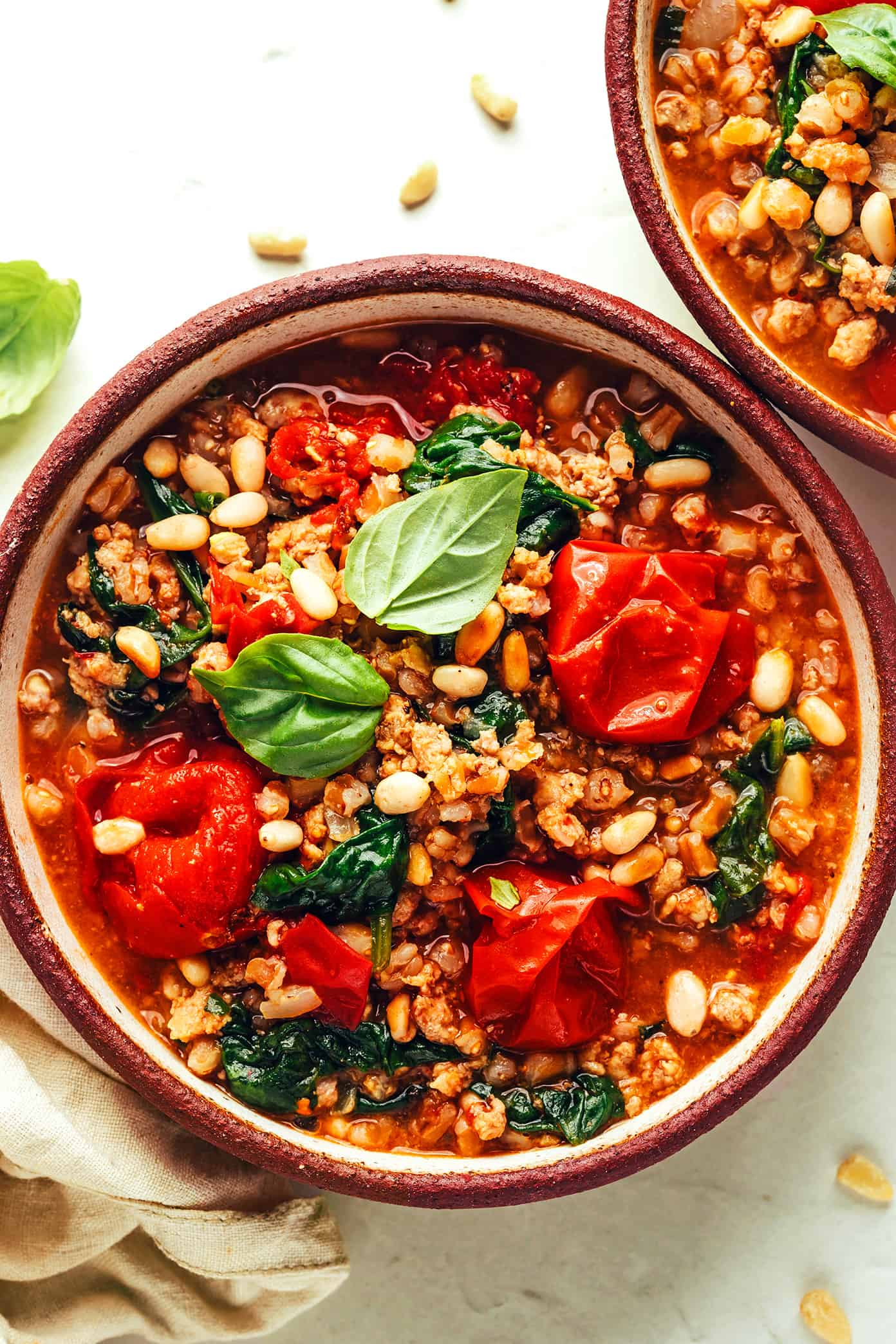 This one pot farro recipe is slow-simmered with Italian sausage, cherry tomatoes, fresh basil, garlic, spinach and finished with a sprinkling of pine nuts and Parmesan. Such an easy dinner recipe and always SO delicious. Feel free to use plant-based sausage to make it vegetarian too! | gimmesomeoven.com One Pot Farro in Bowls with Pine Nuts