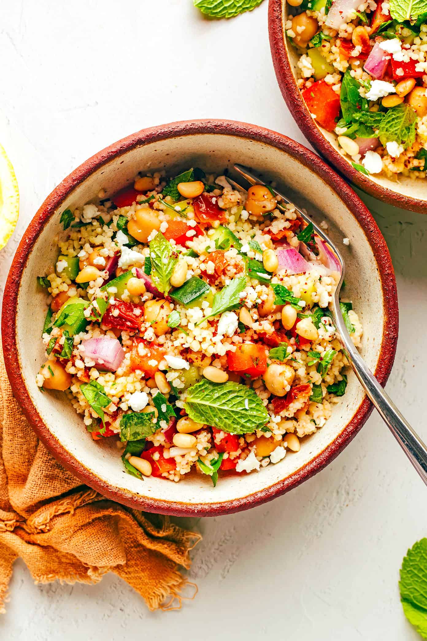 This simple couscous salad is made with loads of fresh veggies (cucumber, bell pepper, red onion), chickpeas, fresh mint and parsley, feta cheese, toasted pine nuts, and a zesty lemon dressing. Feel free to add in some chicken, salmon or shrimp in there too if you'd like. It's the perfect vegetarian entree or side salad...and tastes great for leftovers the next day! | gimmesomeoven.com Serving bowls of couscous salad
