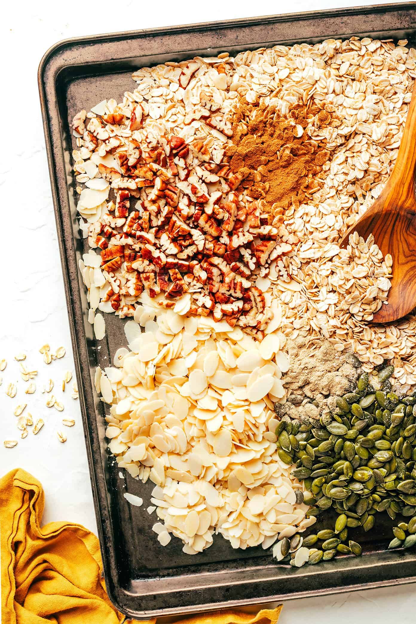 This delicious homemade muesli recipe is easy to make and customize with your favorite blend of oats, nuts, seeds, dried fruit, coconut (optional) and spices. Serve with hot or cold milk, prep "overnight oats"-style, layer as a parfait with Greek yogurt, or however you love best. Always such a great healthy and easy breakfast! | gimmesomeoven.com Muesli oats, nuts, and spices on baking sheet