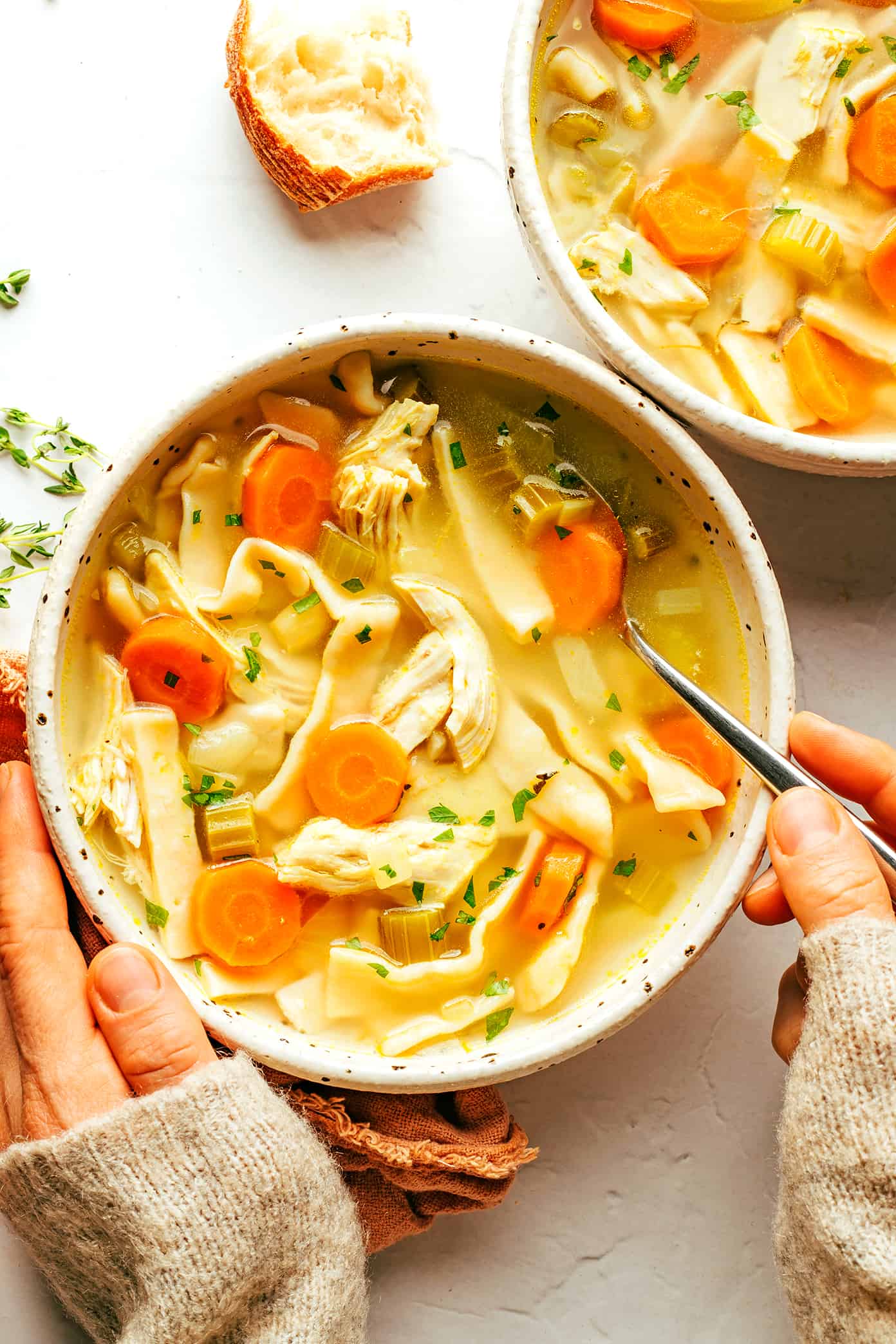 This homemade chicken noodle soup recipe is made with homestyle egg noodles, tender chicken, thick-cut veggies, and the coziest garlic-herb broth. The perfect comfort food to warm you right up! | gimmesomeoven.com Bowls of homemade chicken noodle soup with bread