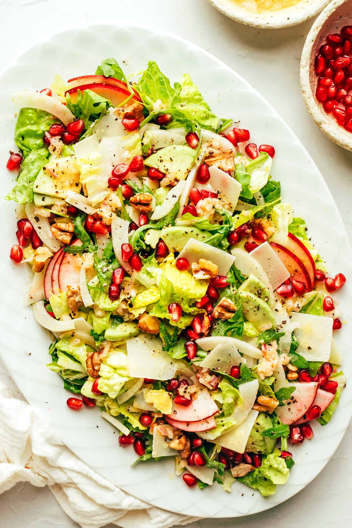 My favorite holiday green salad is tossed with arugula, pomegranate, apple, fennel, toasted walnuts, Parmesan and a simple shallot vinaigrette. Perfect for Thanksgiving, Christmas, or any winter weeknight that you're craving a fresh and delicious salad. | gimmesomeoven.com Thanksgiving Green Salad on platter (with pomegranate, apple, avocado, Parmesan, fennel and walnuts)