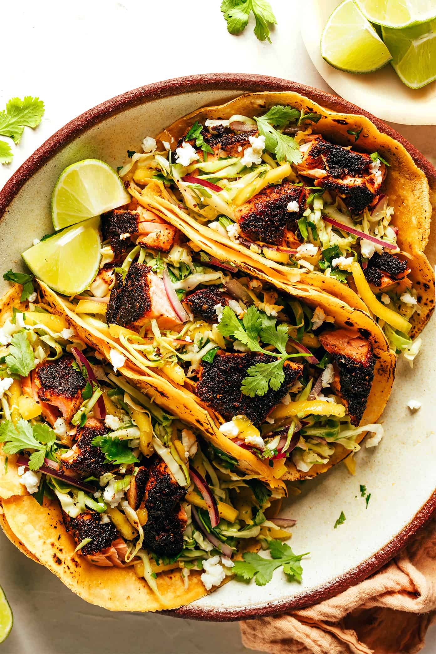 This blackened salmon tacos recipe is layered with a quick mango slaw, corn tortillas, and your choice of zesty toppings. Quick and easy to prepare, naturally gluten-free, and always such a delicious and healthy dinner recipe! | gimmesomeoven.com Blackened Salmon Tacos on Plate