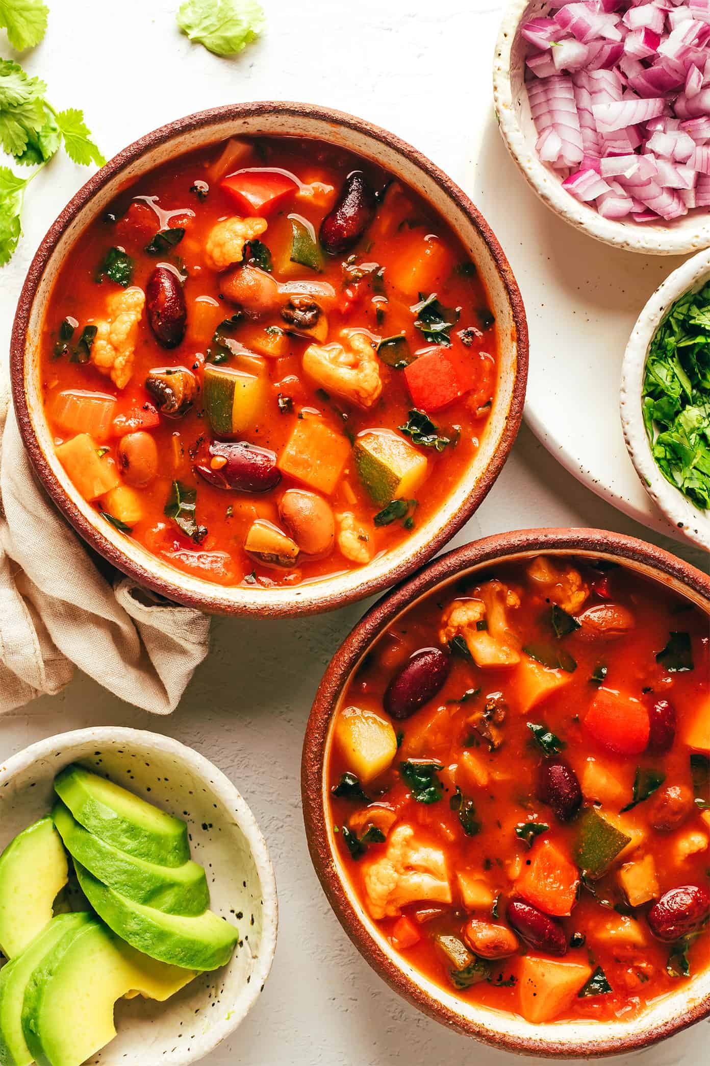 This delicious vegetarian chili recipe is easy to make, full of rich flavor, and loaded up with your choice of beans and veggies (such as sweet potato, bell pepper, zucchini, mushrooms, cauliflower, etc). This soup recipe is naturally gluten-free and vegan, very customizable, and always SO delicious. | gimmesomeoven.com Bowls of vegetarian chili