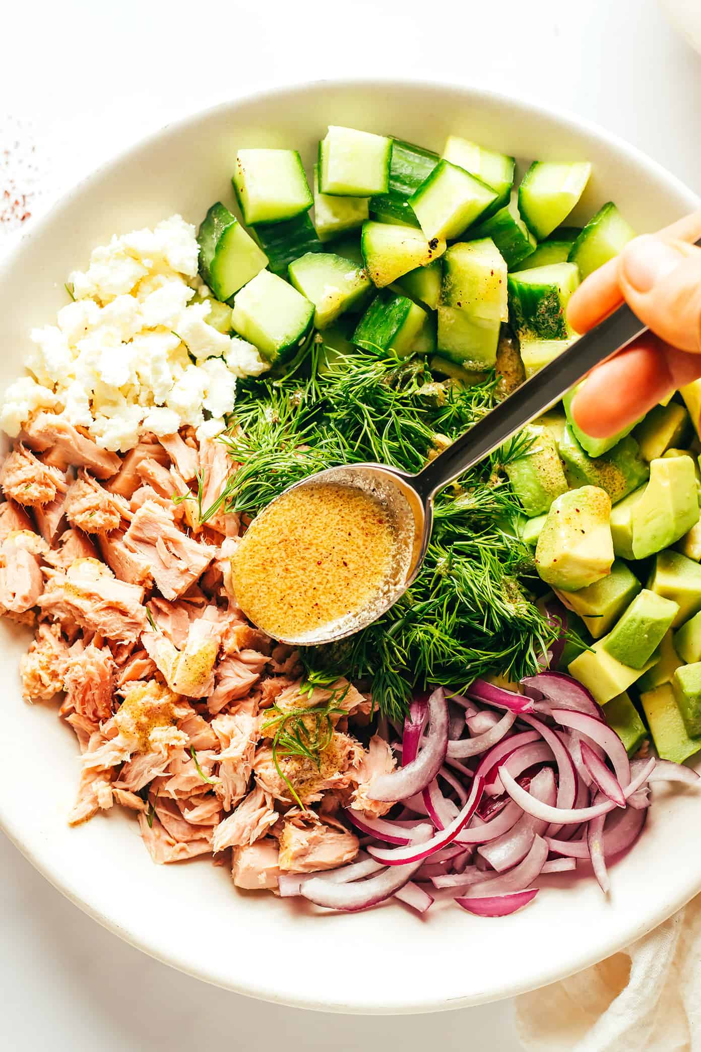 This simple tuna salad is tossed with avocado, cucumber, feta, red onions, herbs and a zippy lemon-sumac dressing and served over brown rice. Easy to make in about 30 minutes, naturally gluten-free, easy to meal prep in advance for lunch or dinner, and always SO delicious. | gimmesomeoven.com Adding lemon dressing to Tuna Avocado Salad