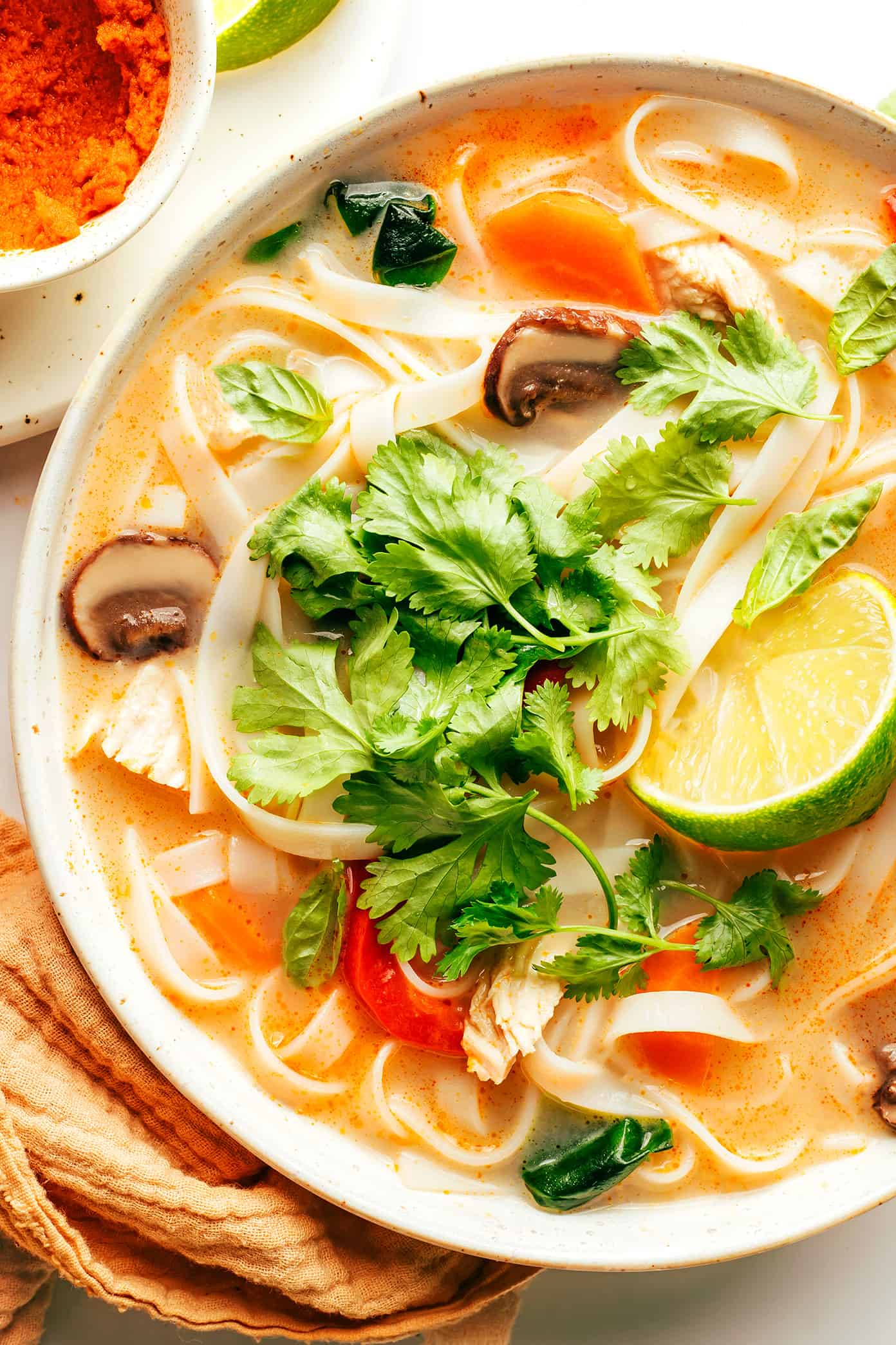 This Thai-inspired chicken noodle soup recipe is quick and easy to make, naturally gluten-free, always tastes so fresh and flavorful! Use whatever protein (chicken, beef, pork, shrimp, tofu, chickpeas), veggies, greens, and noodles you happen to have on hand, simmer everything together in a ginger coconut curry broth, top with fresh herbs and lime and dinner is ready to go! | gimmesomeoven.com Bowl of Thai Chicken Noodle Soup