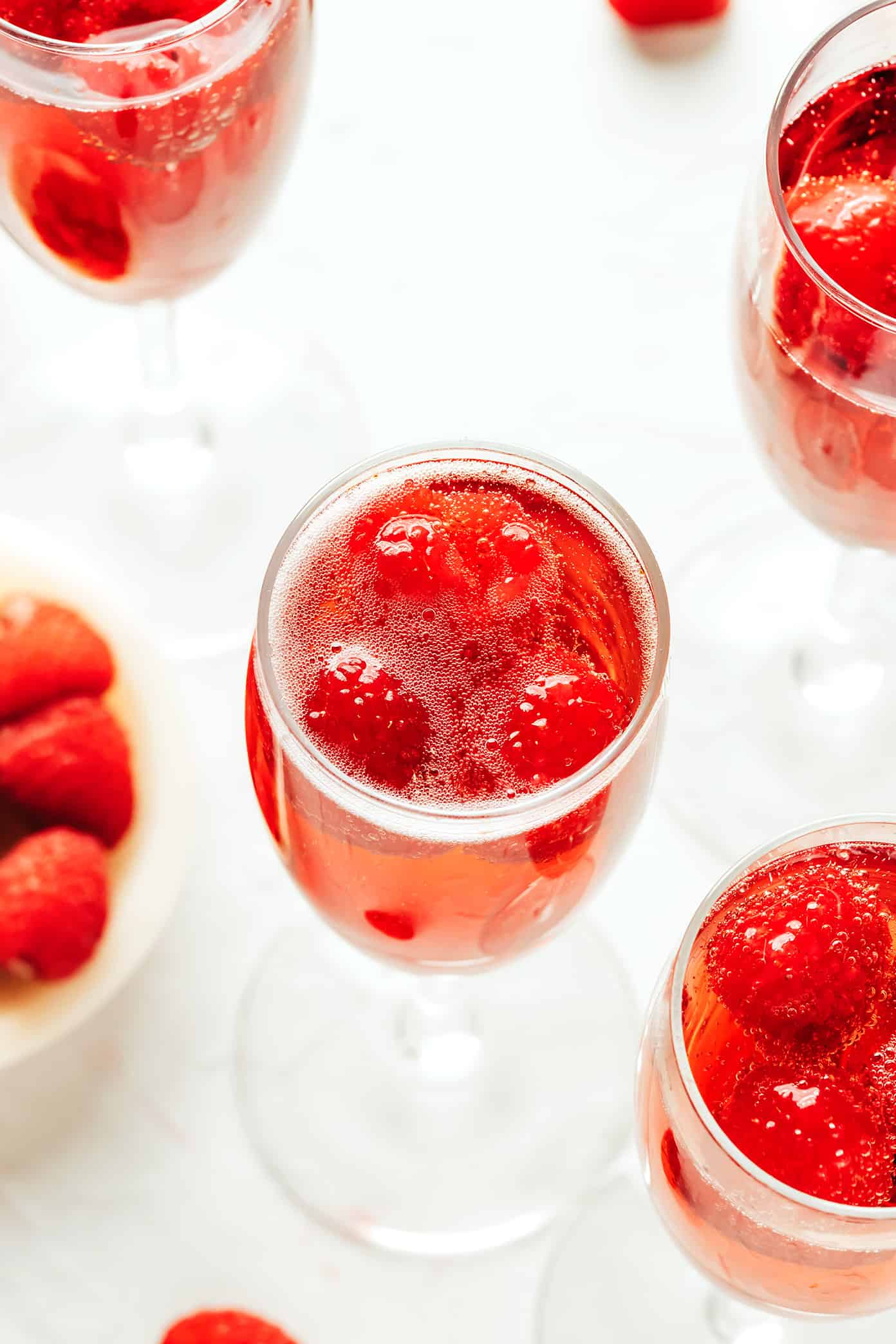 This classic kir royale cocktail recipe is easy to make with dry sparkling wine (such as Champagne, cava or prosecco), crème de cassis (blackcurrant liqueur) and your choice of berries for garnish. It's a vibrant, bubbly, refreshing drink that's perfect for summertime! | gimmesomeoven.com Closeup of kir royale drinks