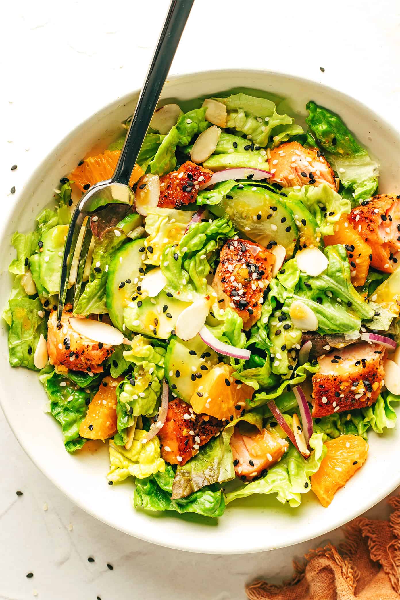 This orange salmon salad recipe is tossed with avocado, cucumber, red onion, toasted almonds, Romaine and drizzled with an irresistible ginger hot honey vinaigrette. It's the perfect sweet and savory entrée salad when you're craving a healthy dinner and it's naturally gluten-free as well. | gimmesomeoven.com Orange Salmon Salad in serving bowl with ginger hot honey vinaigrette