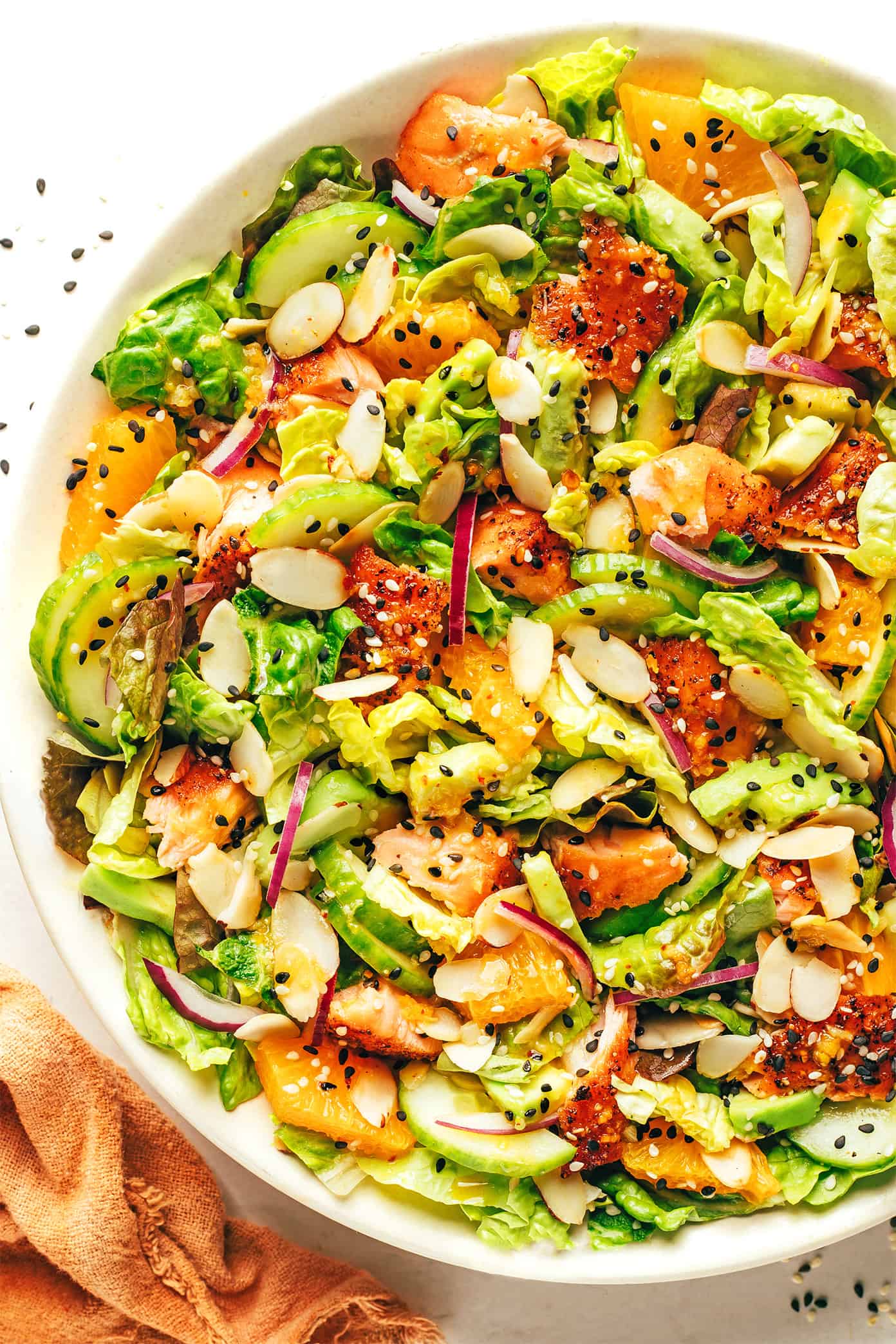 This orange salmon salad recipe is tossed with avocado, cucumber, red onion, toasted almonds, Romaine and drizzled with an irresistible ginger hot honey vinaigrette. It's the perfect sweet and savory entrée salad when you're craving a healthy dinner and it's naturally gluten-free as well. | gimmesomeoven.com Orange salmon salad with avocado and toasted almonds in serving bowl
