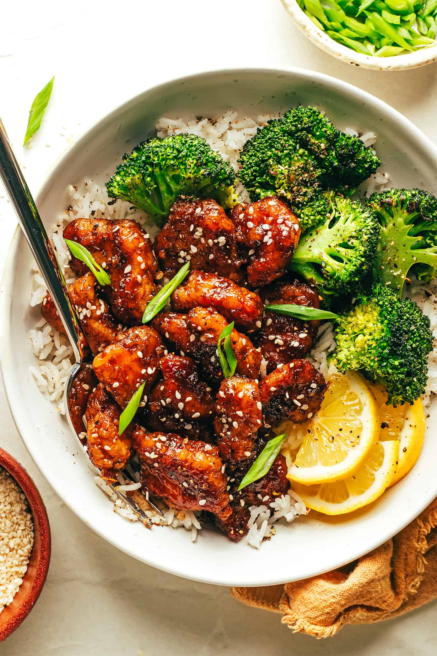 This Chinese inspired sticky honey lemon chicken recipe is easy to make and tossed with an irresistible 5-ingredient stir fry sauce. Serve with rice or noodles and feel free to swap beef, pork, shrimp or tofu for chicken if you prefer. Always a delicious and easy dinner recipe! | gimmesomeoven.com Sticky honey lemon chicken in bowl with roasted broccoli rice and lemon