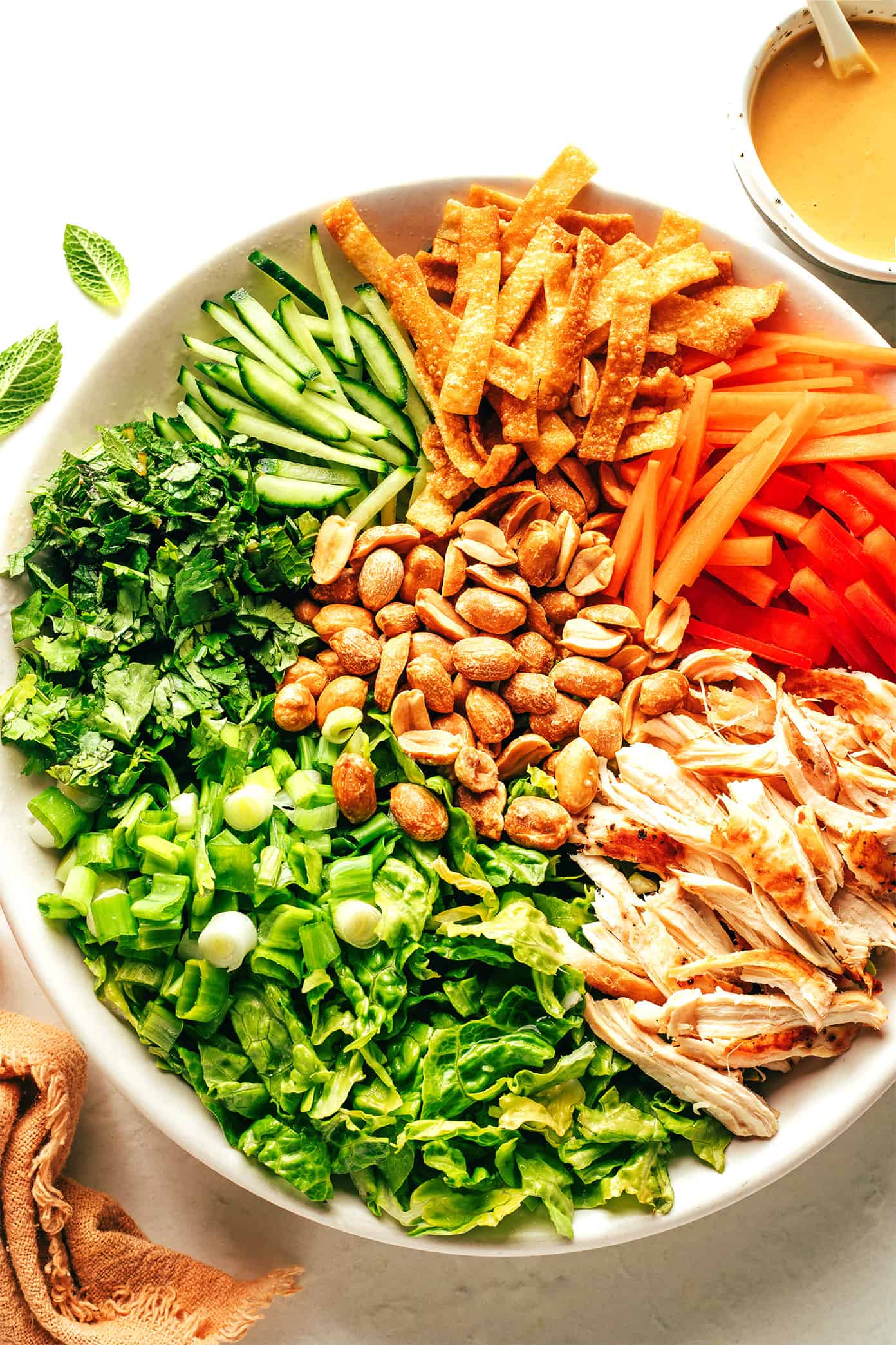 This Thai-Inspired chopped salad is made with loads of fresh veggies and cabbage, crispy wonton strips, shredded chicken (or shrimp, salmon, pork), and an irresistible creamy peanut dressing. Feel free to swap in roasted chickpeas to make this salad vegetarian, or leave out the additional protein altogether. So fresh and flavorful!! | gimmesomeoven.com Thai salad ingredients in bowl