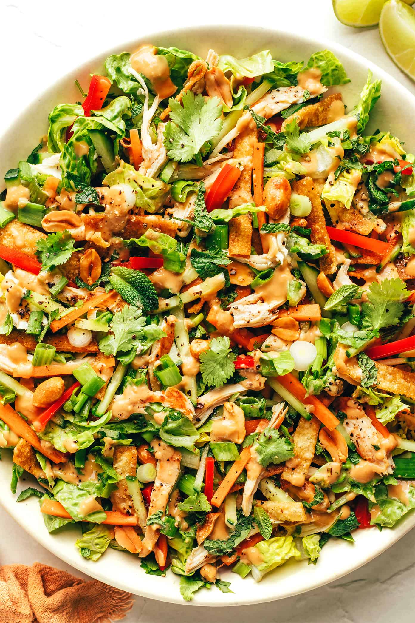 This Thai-Inspired chopped salad is made with loads of fresh veggies and cabbage, crispy wonton strips, shredded chicken (or shrimp, salmon, pork), and an irresistible creamy peanut dressing. Feel free to swap in roasted chickpeas to make this salad vegetarian, or leave out the additional protein altogether. So fresh and flavorful!! | gimmesomeoven.com Thai Crunch Salad in bowl drizzled with peanut dressing
