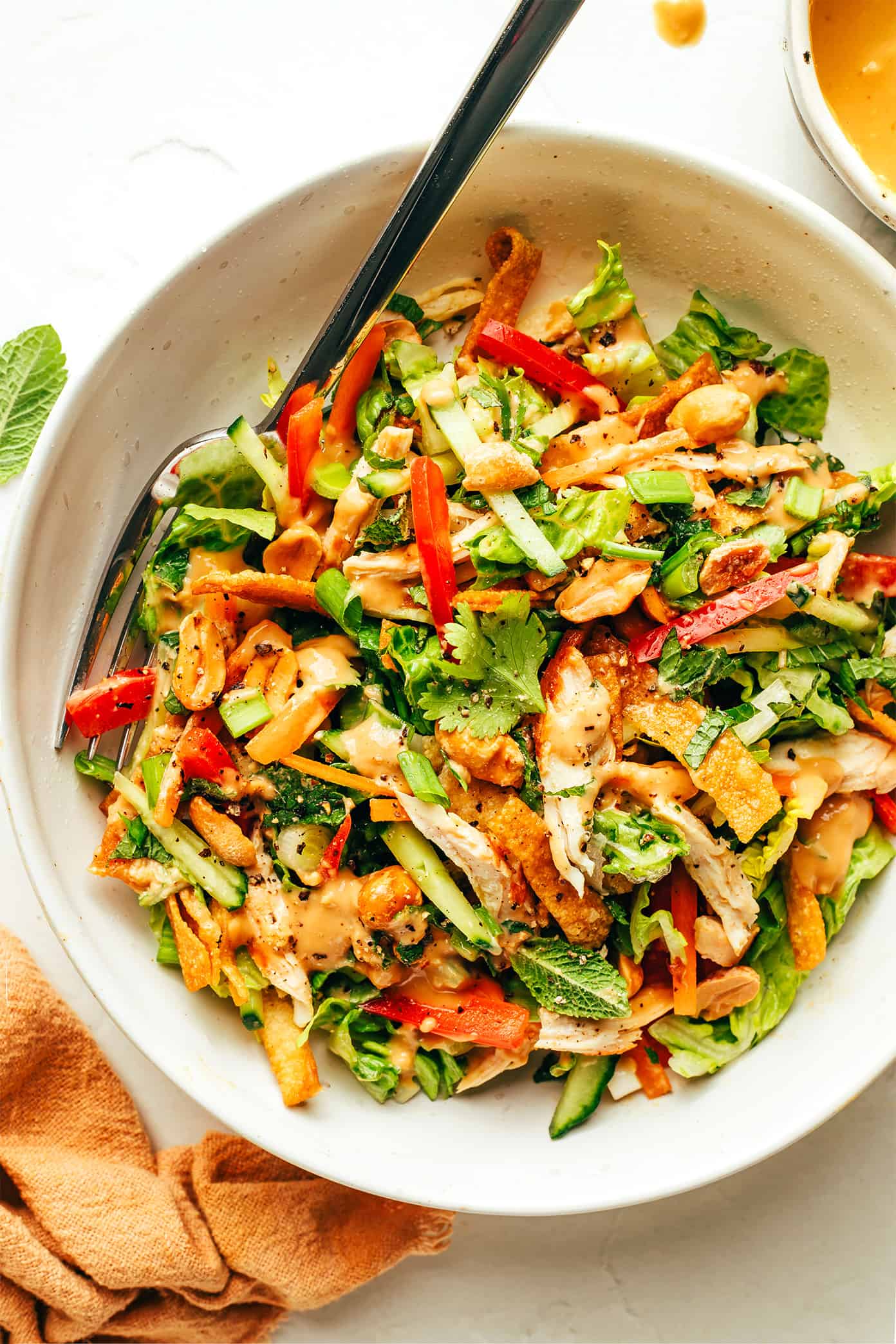 This Thai-Inspired chopped salad is made with loads of fresh veggies and cabbage, crispy wonton strips, shredded chicken (or shrimp, salmon, pork), and an irresistible creamy peanut dressing. Feel free to swap in roasted chickpeas to make this salad vegetarian, or leave out the additional protein altogether. So fresh and flavorful!! | gimmesomeoven.com Thai Crunch Salad drizzled with peanut dressing in bowl with fork