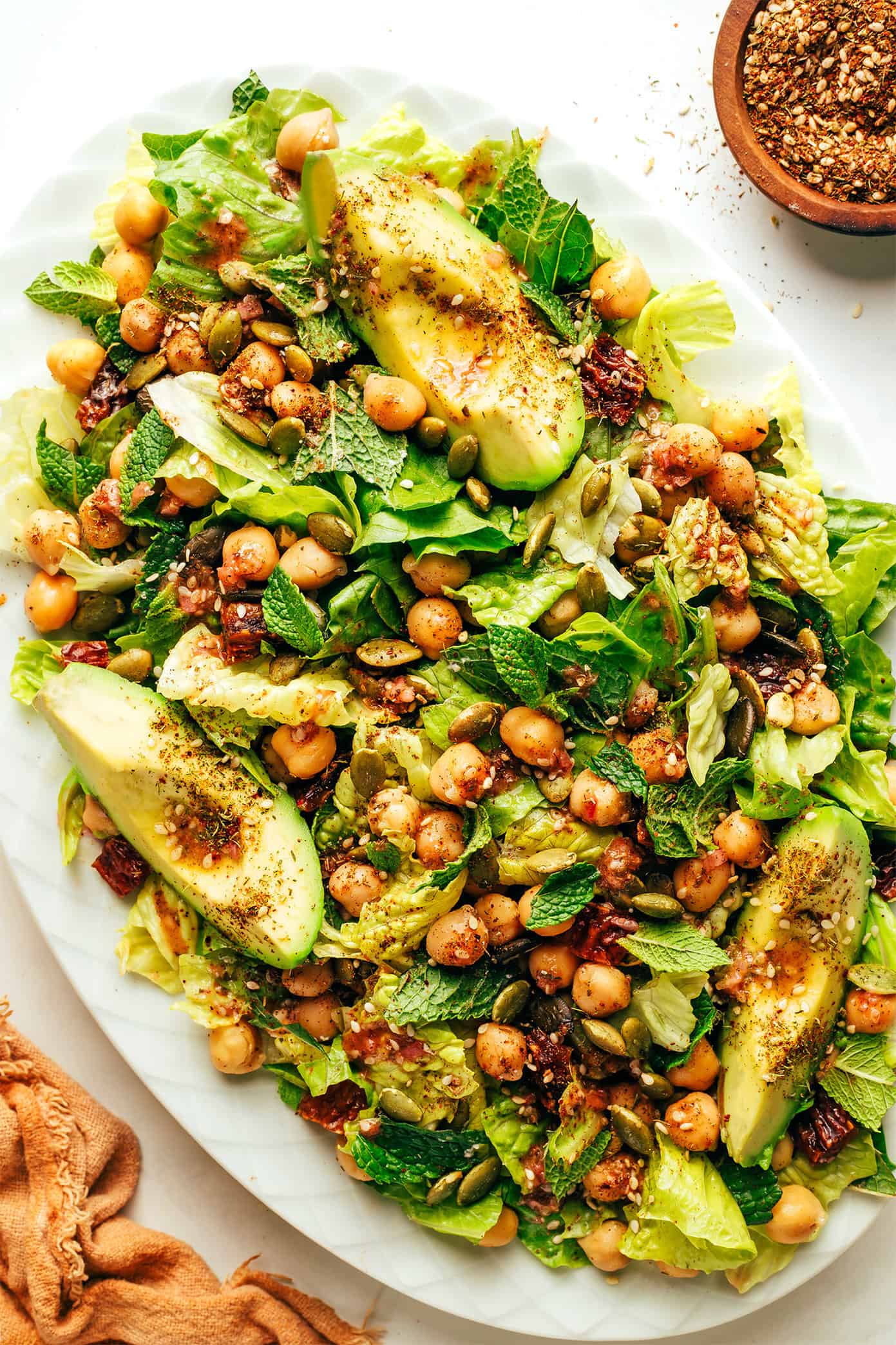 This vibrant green salad is loaded up with chickpeas, Medjool dates, avocado, pepitas, loads of fresh mint, and tossed with a lemony za'atar shallot vinaigrette. It's naturally vegan and gluten-free, but feel free to add a protein such as chicken, steak, shrimp or salmon if you'd like. So fresh and delicious! | gimmesomeoven.com Chickpea, Date and Avocado Salad with Za'atar Vinaigrette on serving platter