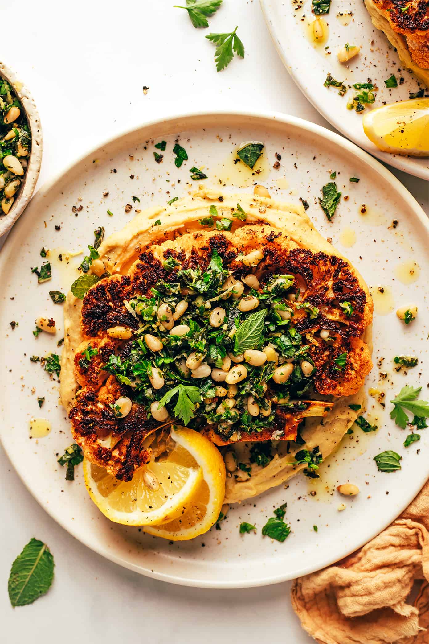 Zesty cauliflower steaks are served over hummus and sprinkled with a lemon-mint pine nut gremolata. A simple, healthy and absolutely delicious dinner recipe that also happens to be vegetarian, vegan and gluten-free. | gimmesomeoven.com Cauliflower Steaks with Hummus and Gremolata on Serving Plates