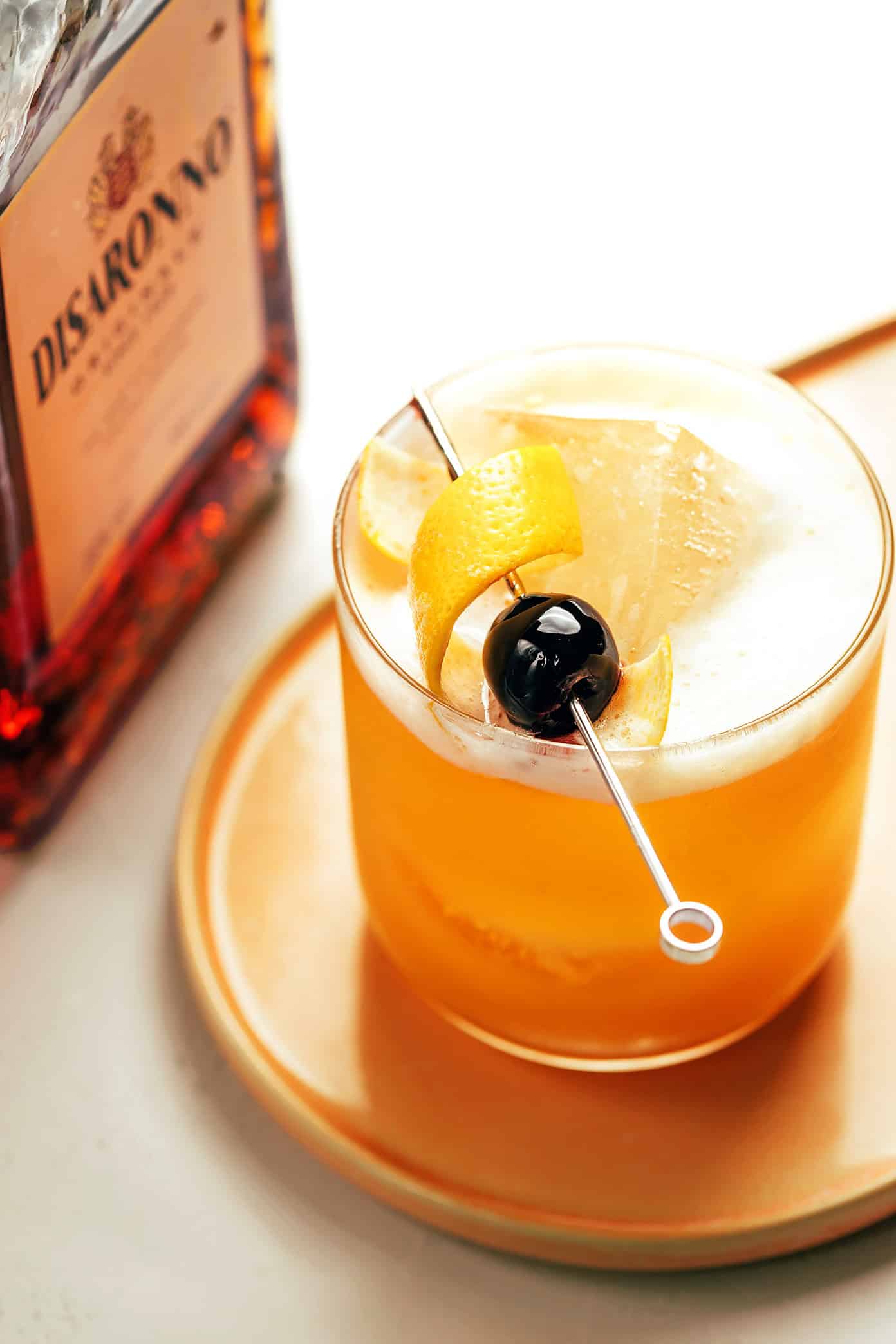 This classic Amaretto Sour recipe is easy to make with bourbon, lemon juice, Amaretto and egg white. Feel free to add additional sweetener or bitters, if you'd like, and garnish with a lemon twist and maraschino cherry. It's always such a cozy and sophisticated cocktail! | gimmesomeoven.com Amaretto Sour Drink